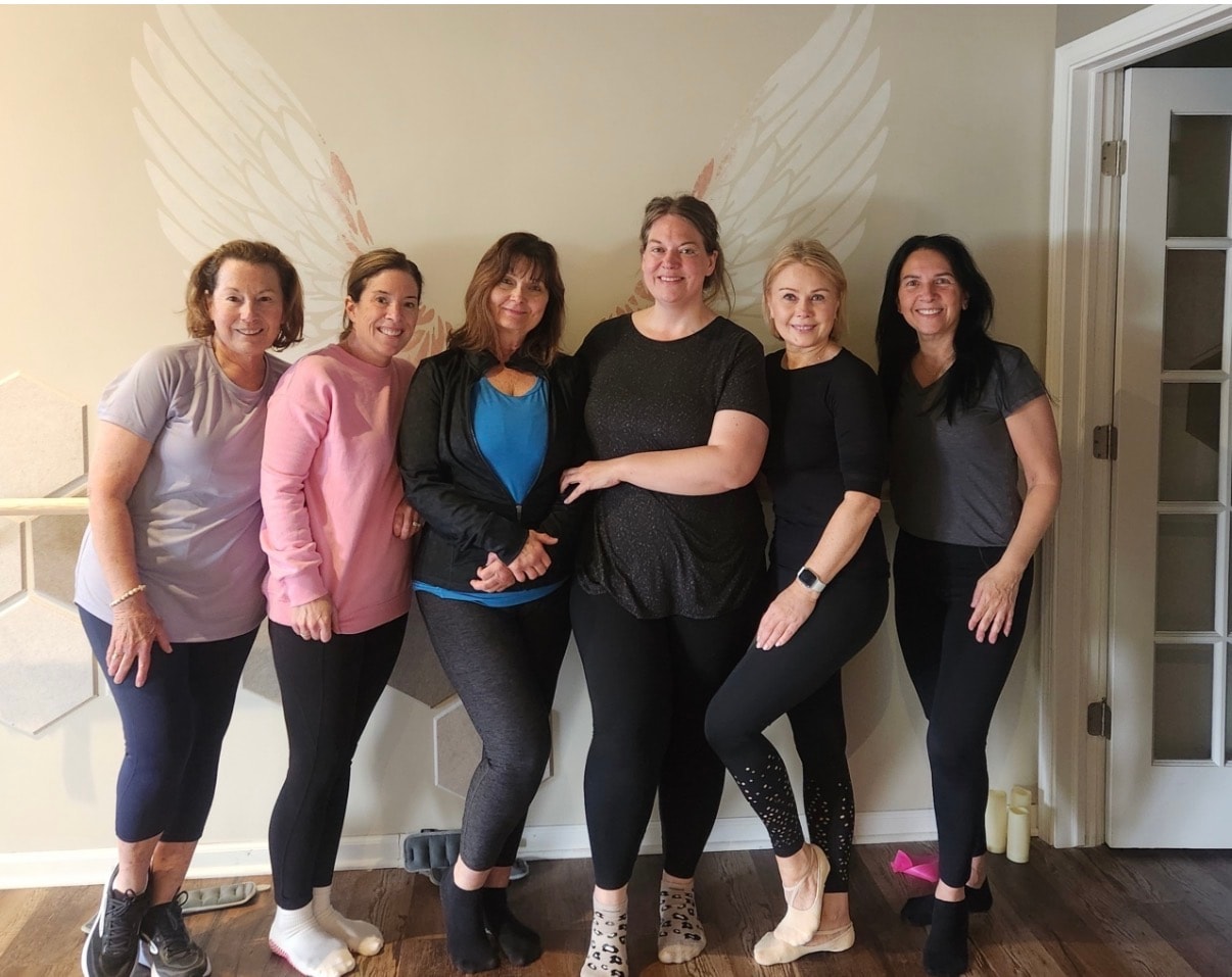 Six women in workout clothes posing in front of the angel wings mural