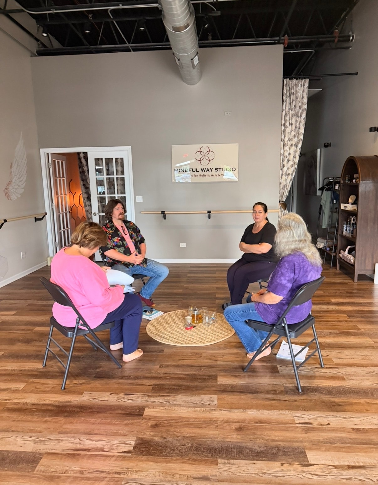 Four people seated in a circle at the Mindful Way Studio sign