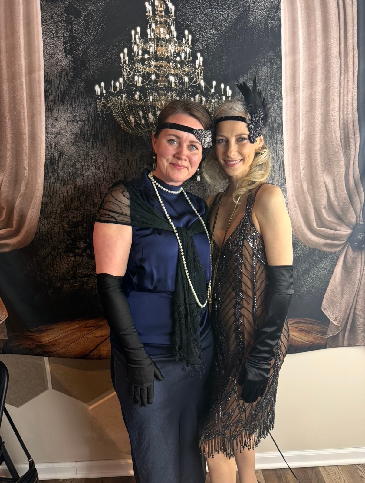 Two women in Gatsby costumes in front of chandelier backdrop