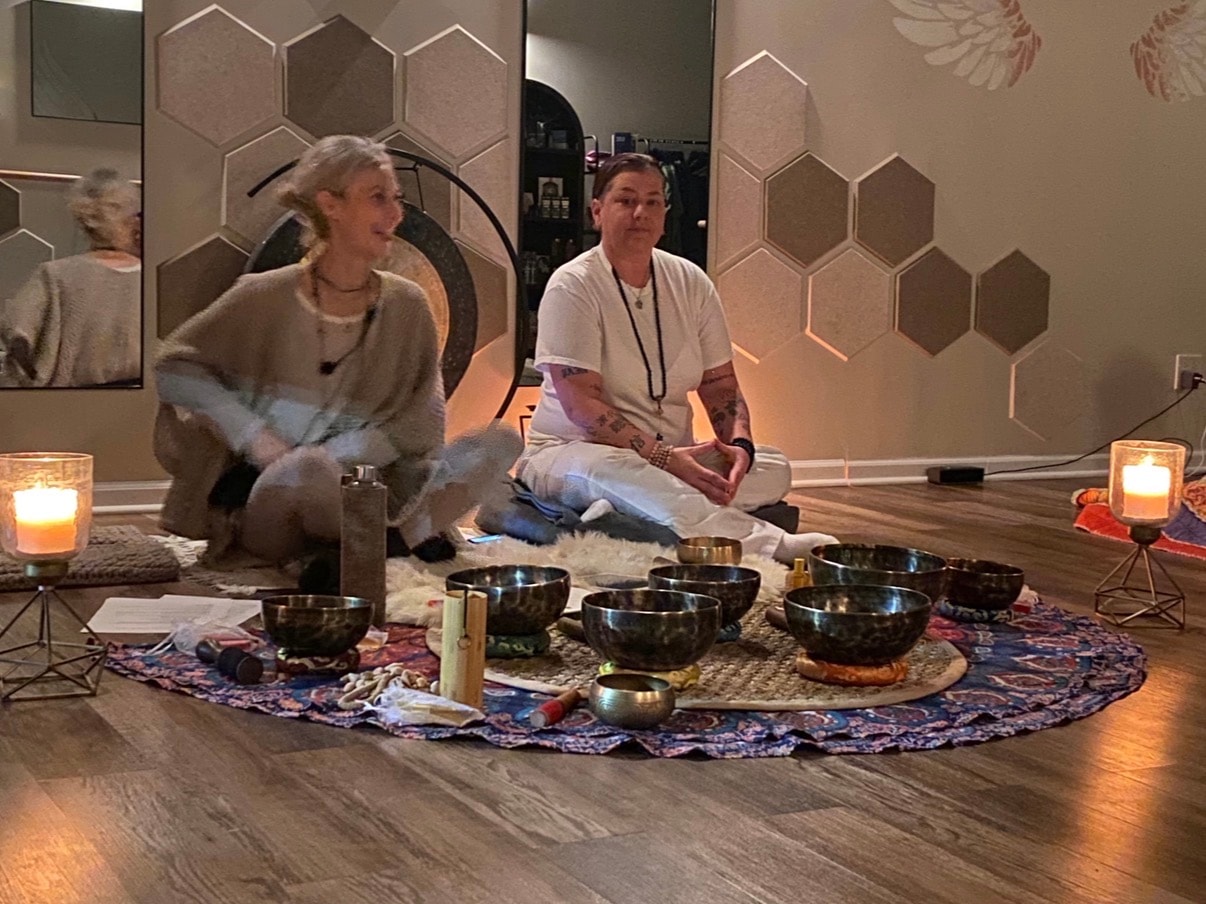Two practitioners seated with Tibetan singing bowls by candlelight