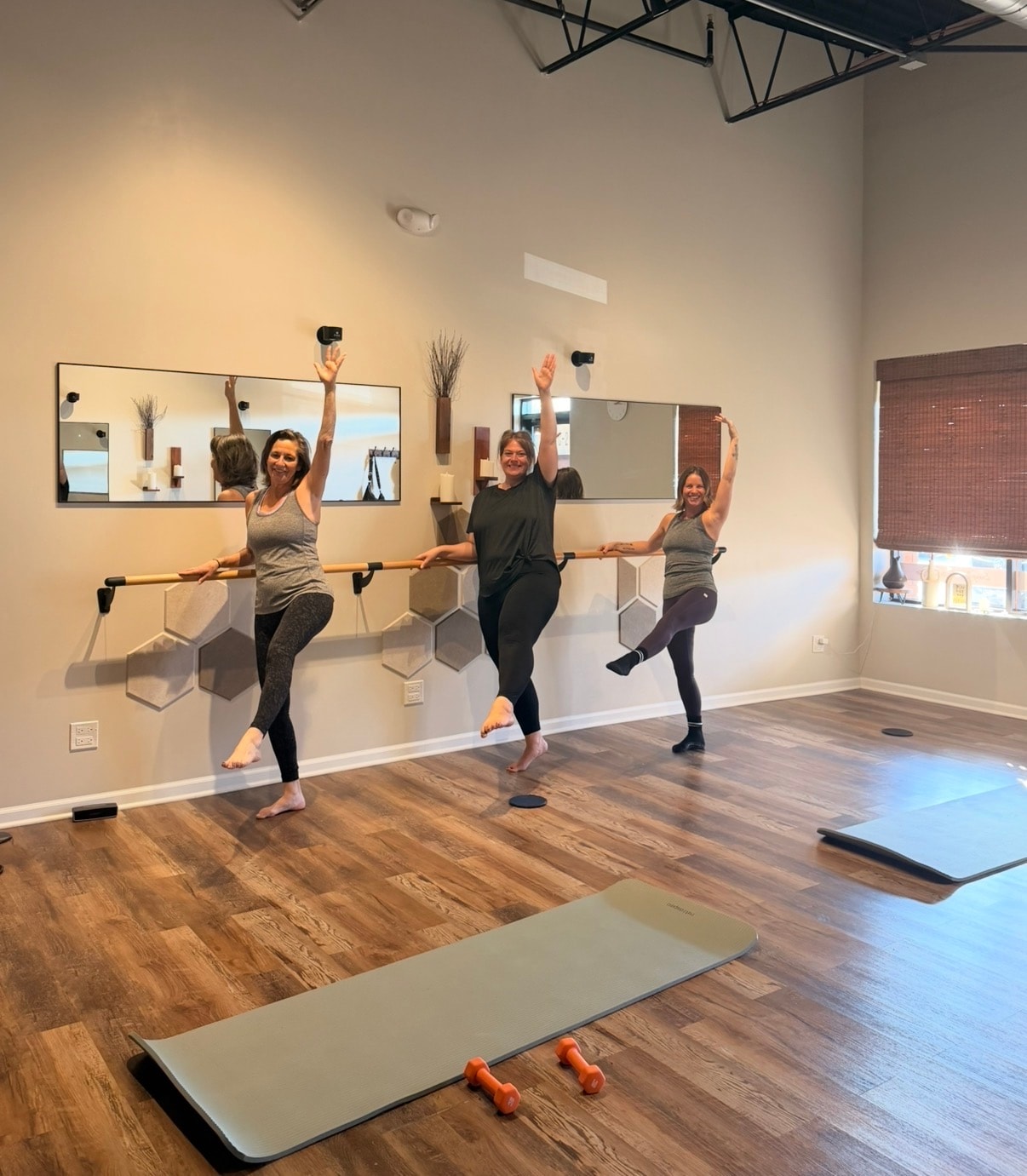 Three women at the barre balancing on one leg and laughing