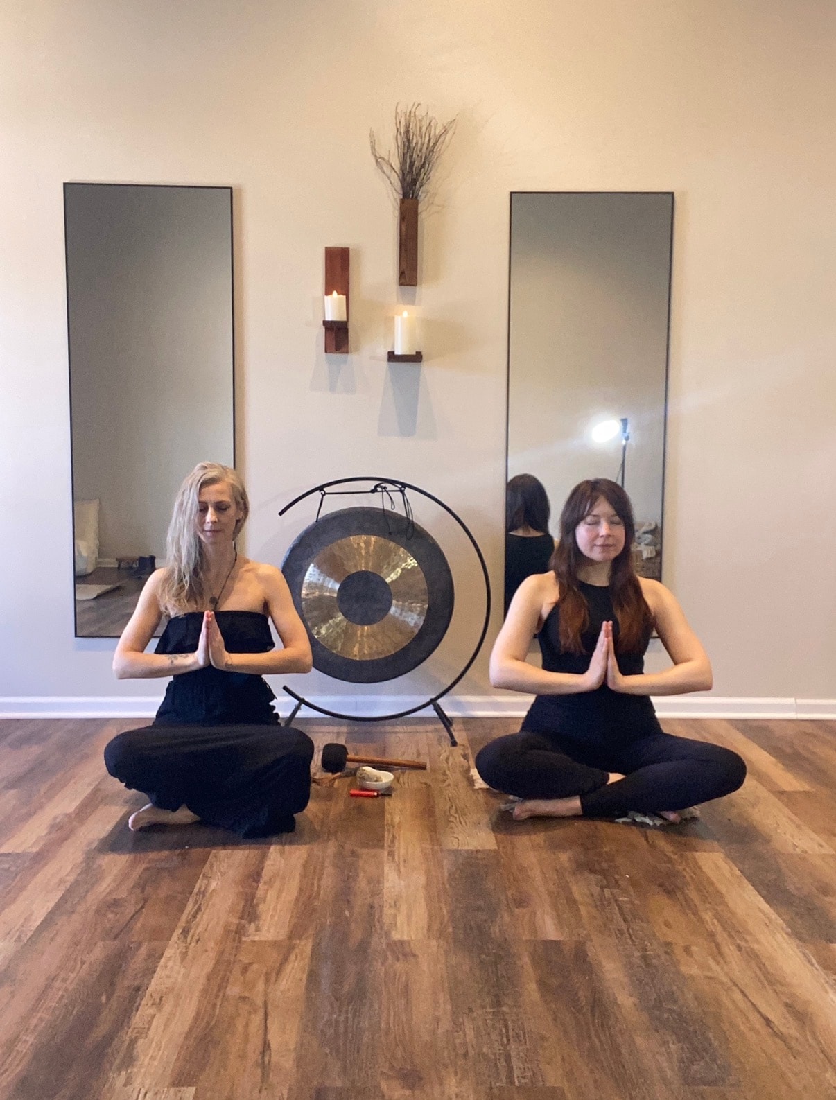 Two women in prayer pose seated in front of the gong