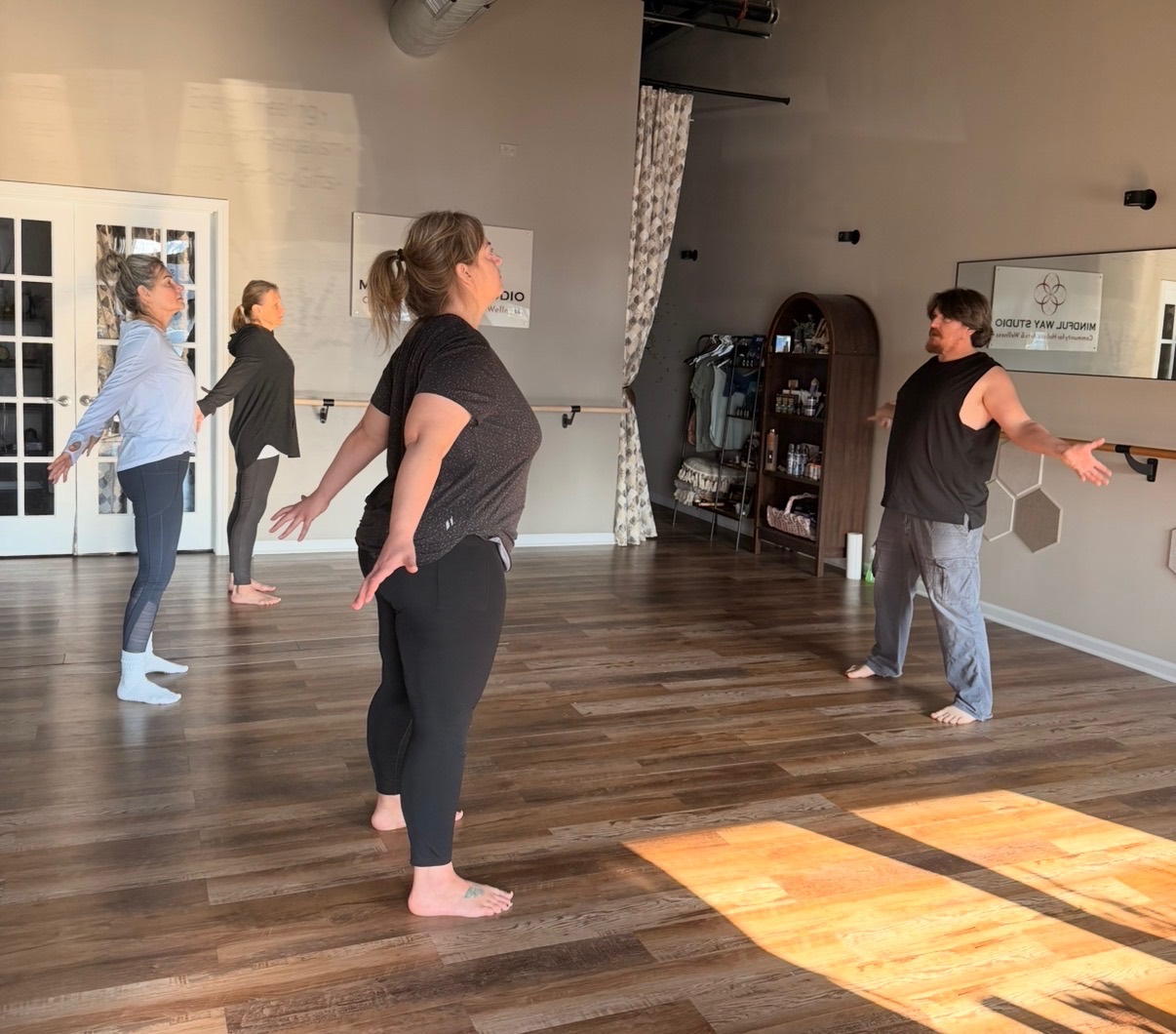 Qigong class at Mindful Way Studio Mokena IL — Shaun leading students through flowing movement with warm morning light on hardwood floors